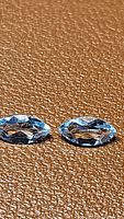 Pair of natural sky blue topaz marquis cut gemstones laid on brown textured surface, highlighting their clarity and faceting.