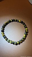 Full view of natural yellow tigerseye stretchy bracelet laid flat on brown surface. Shows coloration and round beads.