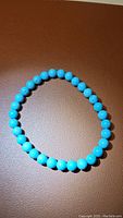 Top view of natural robin's egg blue turquoise bracelet laid flat on a brown surface, showing round turquoise beads.