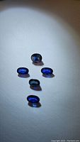 Five oval cut royal blue sapphires arranged on white background, showing rich blue hues and natural surface inclusions.