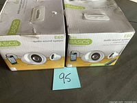 Two boxed Basics E60 audio sound system speakers showing front of packaging and some damage