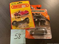 Two Matchbox die-cast metal cars in their original sealed packaging placed on a dark surface.