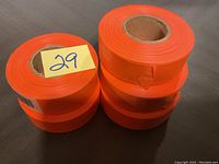 Photo showing 5 rolls of bright orange tape, stacked in two columns on a gray surface.