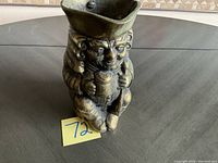 Photo of the brass figurine from front angle showing facial details and held object