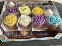 Photo showing an assortment of 24 individual candles in a display box with plastic clear cases. Candles are cupcake and rose flower designs in various colors.