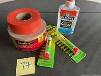 Photo showing the glue and tape lot items including Elmer's clear glue bottle, Scotch paper masking tape roll, and two Krazy Super Glue tubes arranged on a table.