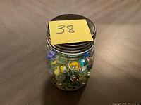 Front view of jar filled with mixed glass marbles with metal lid and sticky note labeled 38.