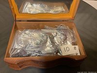 Open wooden jewelry box showing assorted costume jewelry in plastic bags, including bracelets and necklaces.