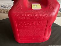 Close-up of embossed warning text on the red gasoline can including flammability warnings and usage instructions.