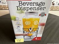 Photo of the packaging showing the beverage dispenser filled with orange liquid and lemon slices inside, includes product claims like rust resistant, leak proof, drip free and food grade material, with a 4 liter capacity.