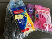 Three pairs of rubber gloves from different brands and types, packaged and displayed on a surface.