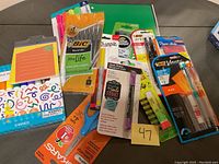 Photo of assorted new school and office supplies including markers, sticky notes, a green notebook, various pens and pencils, and scissors.