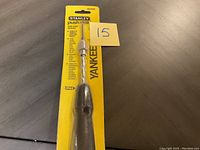 Front view of Stanley push drill in yellow packaging showing drill bit and handle.