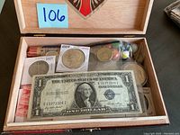 Open wooden box showing contents from above, including paper currency, coins, stamp blocks and marbles