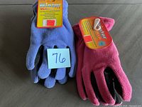 Two Winter Warmth gloves made of blue and pink fleece with attached yellow and orange tags showing brand and features, placed side-by-side on a gray surface