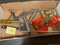 Box containing several metal wrenches, a yellow-handled screwdriver, long metal tool with wooden handle, and two packaged brass hardware items.