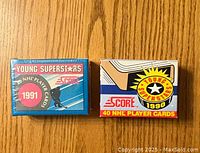 Two unopened sets of Score Young Superstars hockey cards from 1990 and 1991 displayed on a wooden surface.