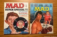 Front covers of the two MAD Magazines side by side on a wooden surface.