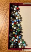 Top-down photo of a collection of various glass marbles in a rectangular box showing many different colors and sizes.