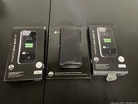 Front view of the lot with two Mophie Juice Pack Air battery cases for iPhone 5/5S/SE and one Motorola phone hip holster still in packaging.