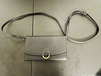 Front view of the black clutch purse showing the gold ring accent on flap closure and attached adjustable shoulder strap.