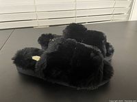 Side and top angle view of black fluffy sandals showing crisscross faux fur design and thick sole.