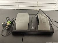 Front angled view of Logitech black and gray gas and brake foot pedals with attached cable and connector showing pedal details and condition.