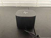 Top and front view of black HP mini desktop computer showing HP logo and attached HDMI cable.