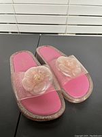 Pair of Kate Spade slide sandals in pink and purple glitter with flower decoration on straps, showing top down view.