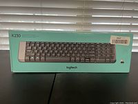 Photo showing Logitech K230 keyboard in original turquoise box with front view of keyboard image.