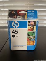 Boxed HP 45 black ink cartridge with white and blue packaging showing flowers, child, and fruits.
