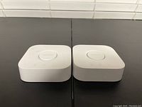 Two Philips Hue smart light hubs placed side by side on a black surface, showing top view with central Philips button visible.