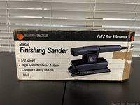 Photo of the front side of the sander box showing Black & Decker branding, model number, and features such as 1/3 sheet size, high speed orbital action, compact and easy to use.