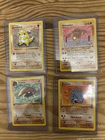 Four 1st Edition Pokemon cards in individual plastic sleeves on a wooden surface.