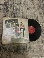 Front view of the vinyl record partially out of its sleeve showing the cover art and the vinyl with red label.