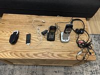 Lot items displayed on wooden table: Apple iPod model 1320, two cordless phones with base stations, three pairs of wired headphones or earbuds.