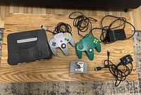 Top view of Nintendo 64 console, grey and green controllers, NASCAR 99 game cartridge and cables including power adapter and AV cable