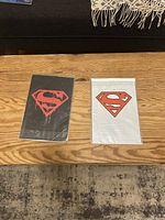 Two sealed comic sets laid side by side on wooden table, one black cover and one white cover, both with Superman logos.