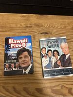 Front cover of the Hawaii Five-0 Season 10 and Diagnosis Murder Season 1 DVD cases side by side on a wooden surface.