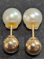 Close-up front view of one pair of reversible stud earrings showing pearl side and gold ball side.