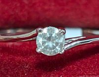 Close-up photo of the round diamond solitaire set in a 10K white gold ring on a red fabric background showcasing the diamond's facets and prong setting.