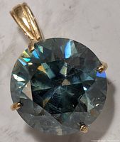Close-up of round greenish-blue moissanite in yellow gold prong setting