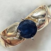 Close-up top view of ring showing round blue sapphire in four-prong setting on polished gold band with chevron detail