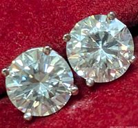 Close-up photo focusing on the two round cut clear moissanite stones set in white gold 4-prong settings on a red background.