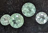 Four round faceted emerald gemstones, showing green color and natural inclusions against a black background.