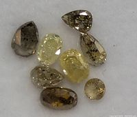 Close-up of eight fancy color diamonds in various yellow and brown hues on white fabric background showing clarity and facets.