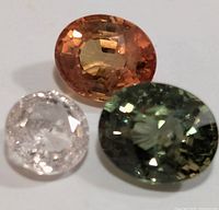 Close-up image of the three loose faceted sapphire gemstones showing their colors and cuts.