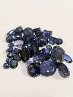 Photo showing a pile of various loose deep blue genuine sapphire gemstones in different shapes and cuts on a white background.