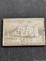 Front side of the silver bar showing an embossed sailing ship and a lighthouse in the background.