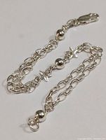 Silver 7 inch bracelet with double link chain, star-shaped charms, spherical ball charms, and lobster clasp laid flat.